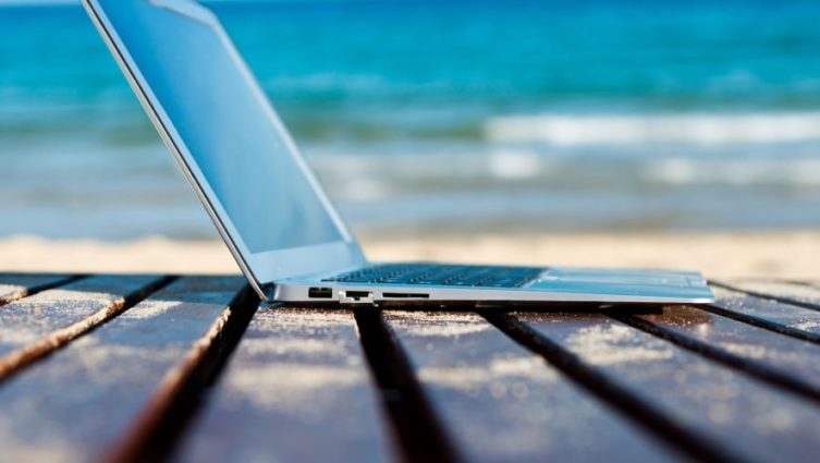 imagem de um computador sobre um deck de madeira com uma praia ao fundo