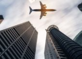 Avião passando por vários prédios em um céu com nuvens