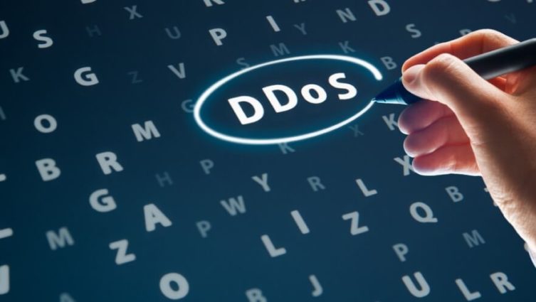 Imagem de uma mão escrevendo sobre uma tela a sigla DDoS