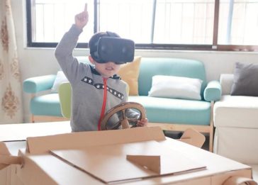 Criança com óculos de realidade virtual brinca em carro feito de papelão - futuro