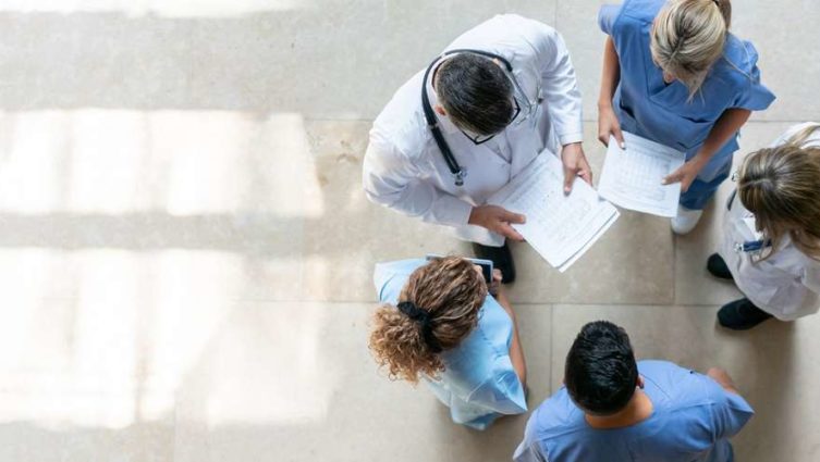 Imagem de uma reunião em círculo de 5 profissionais de saúde em um hospital