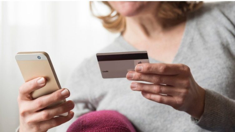 Mulher segura um cartão de crédito com uma mão e o telefone celular com outra mão para fazer um pagamento digital