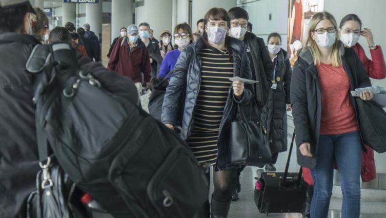 Imagem de pessoas usando máscara no corredor de um aeroporto