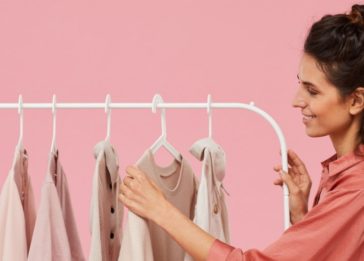 Imagem de mulher escolhendo roupas em uma arara com cabides_indústria têxtil
