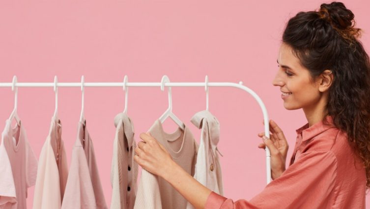 Imagem de mulher escolhendo roupas em uma arara com cabides_indústria têxtil
